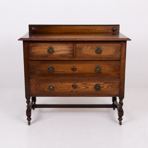 fig 1. An Edwardian oak chest of drawers with two short over two long drawers, brass drop handles, a low backstand, and barley twist legs set on castors.