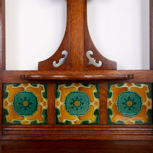 fig 1. A tall Victorian golden oak hallstand featuring an octagonal central mirror, decorative ceramic tiles, brass coat hooks, a single central drawer, and lower umbrella drip trays.
