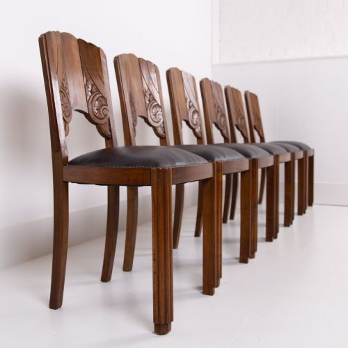 fig 1. A set of four dark walnut dining chairs featuring carved sunburst motifs on the backs and dark leather upholstered seats.