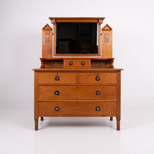 fig 1. An Arts and Crafts oak dressing chest featuring a superstructure with a central mirror, inlaid side panels, and small jewellery drawers above a chest of drawers.