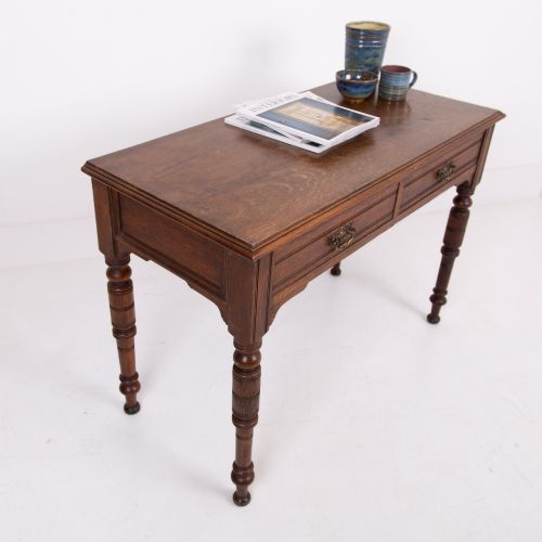 fig 1. A Victorian solid oak writing desk featuring two drawers with brass drop handles and supported by four turned legs.