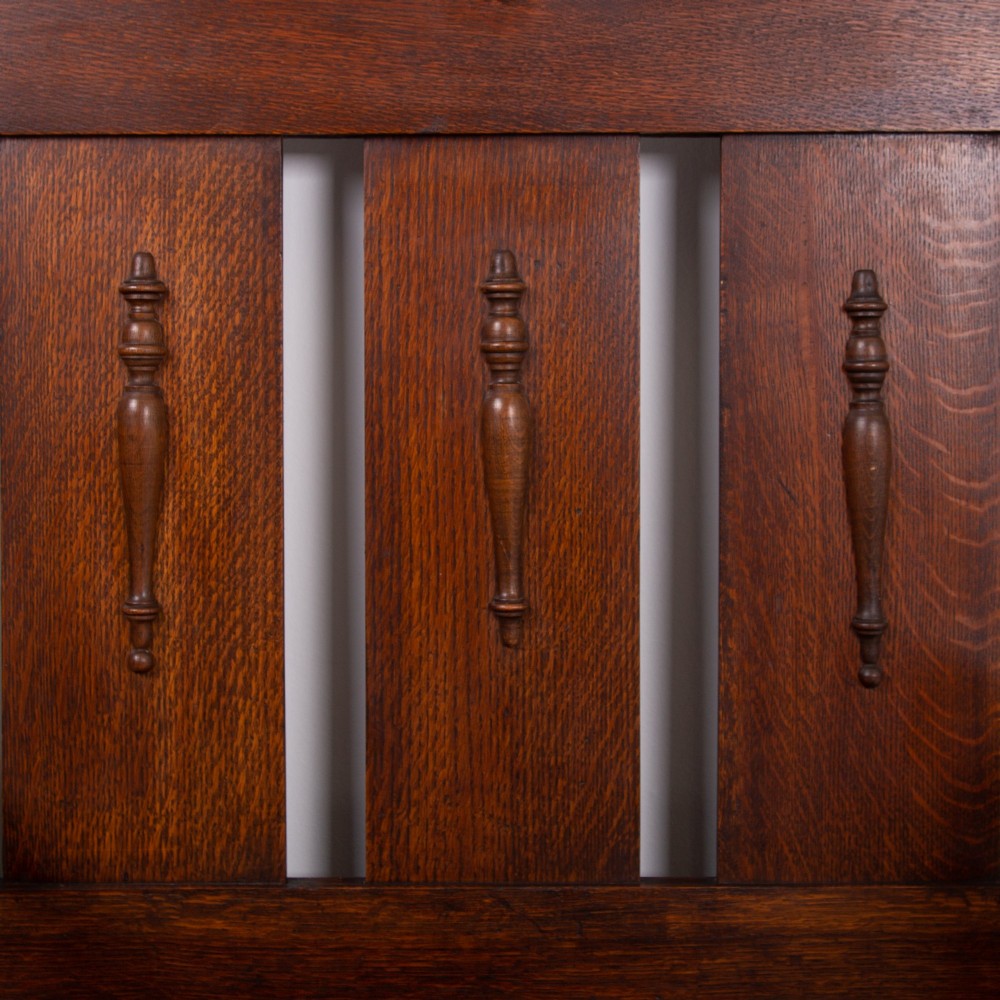An Arts and Crafts oak hallstand featuring a diamond-shaped mirror frame, integrated brass coat hooks, turned spindles, and a seat with lift-top storage. View IV