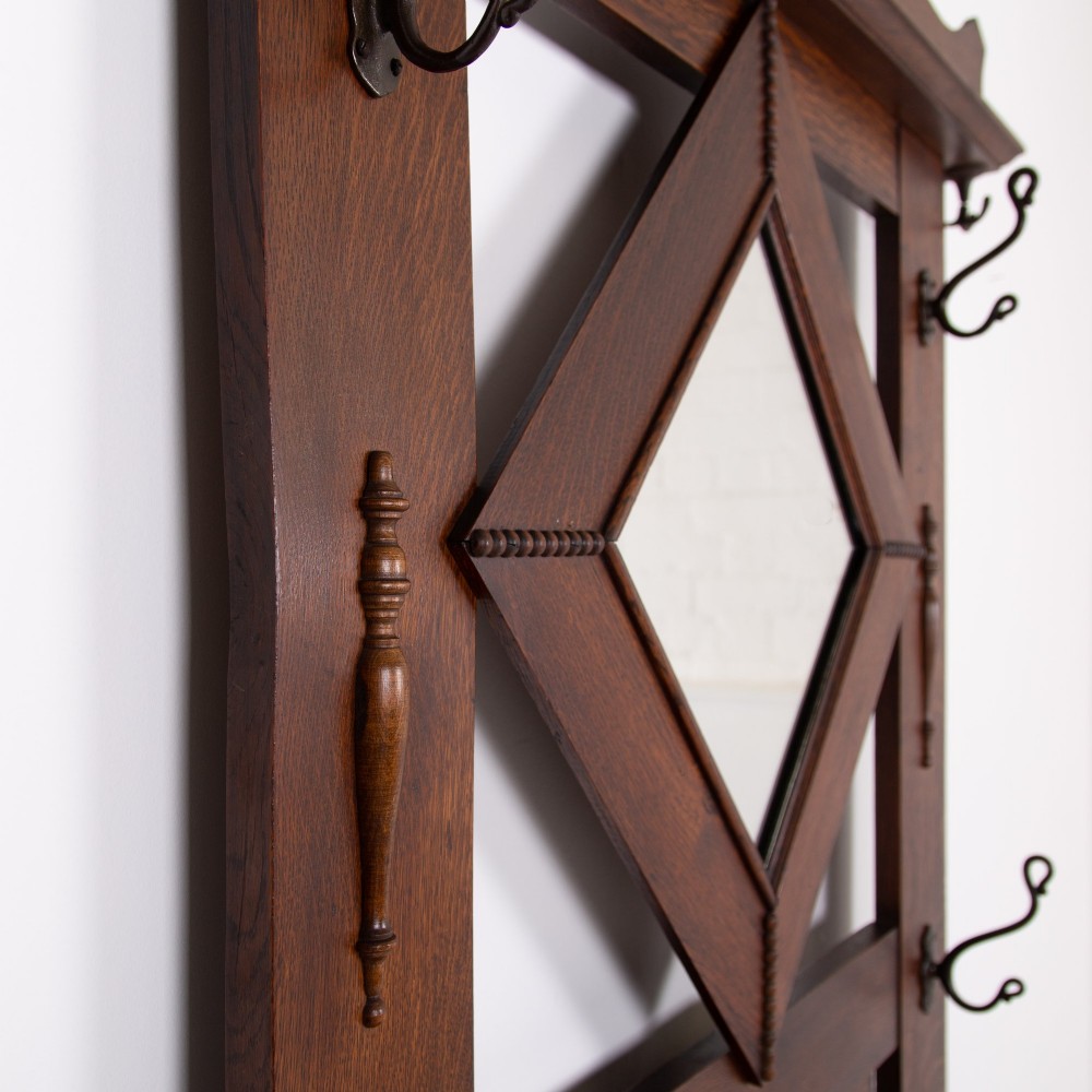 An Arts and Crafts oak hallstand featuring a diamond-shaped mirror frame, integrated brass coat hooks, turned spindles, and a seat with lift-top storage. View V