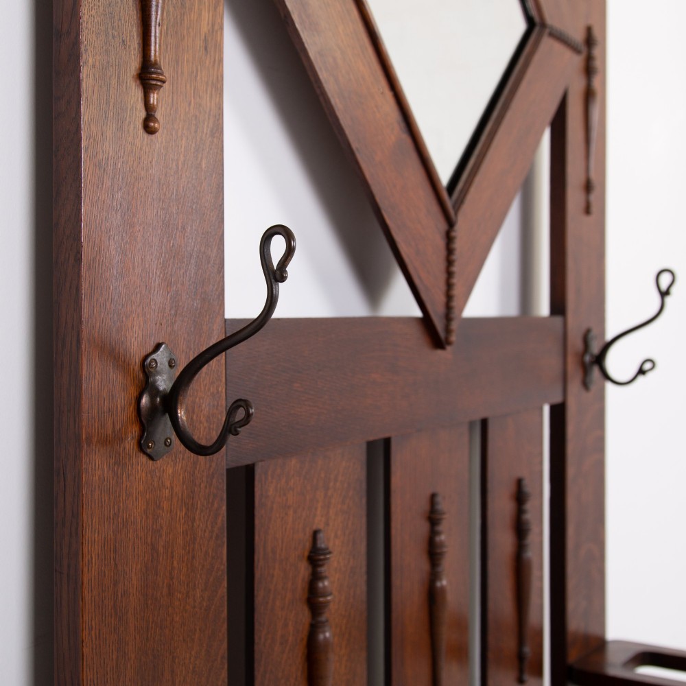 An Arts and Crafts oak hallstand featuring a diamond-shaped mirror frame, integrated brass coat hooks, turned spindles, and a seat with lift-top storage. View VIII