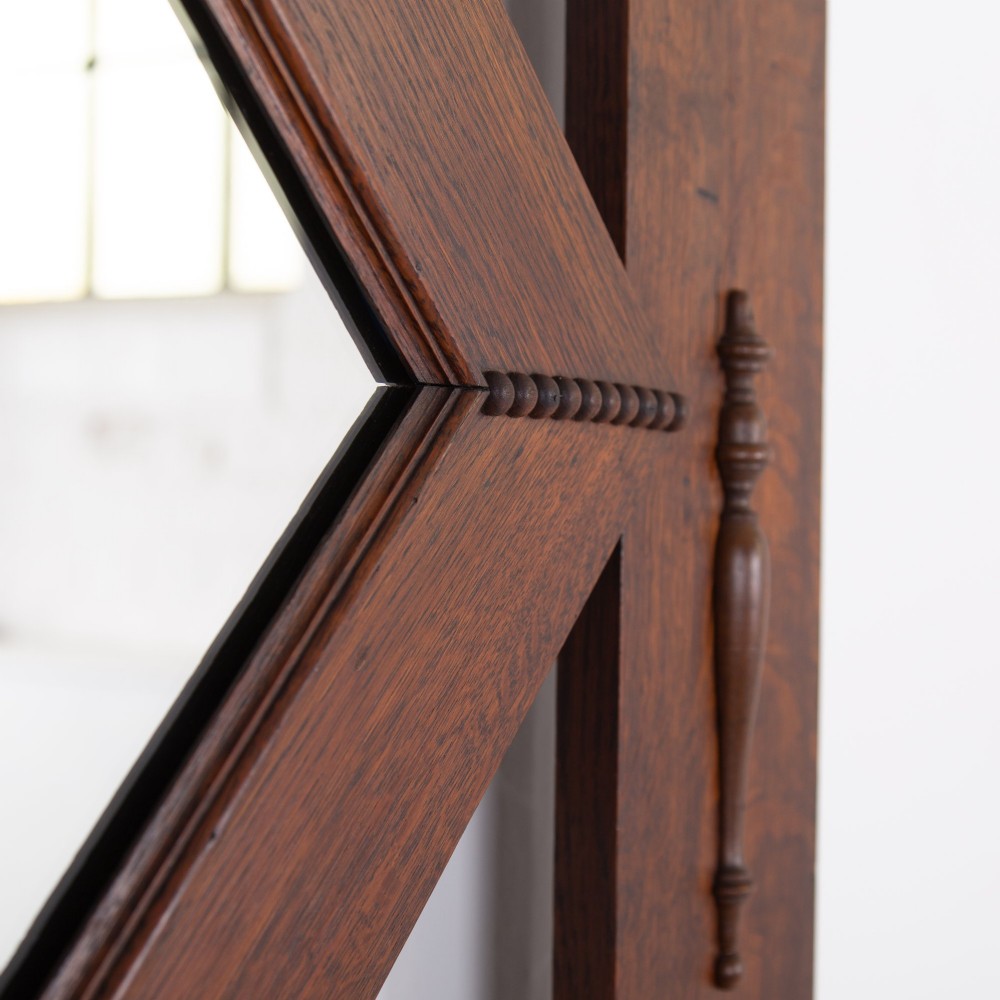 An Arts and Crafts oak hallstand featuring a diamond-shaped mirror frame, integrated brass coat hooks, turned spindles, and a seat with lift-top storage. View XI