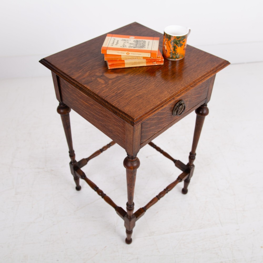 An antique dark oak side table featuring a single drawer with a brass drop ring pull, slender turned legs, and a bobbin stretcher base. View II