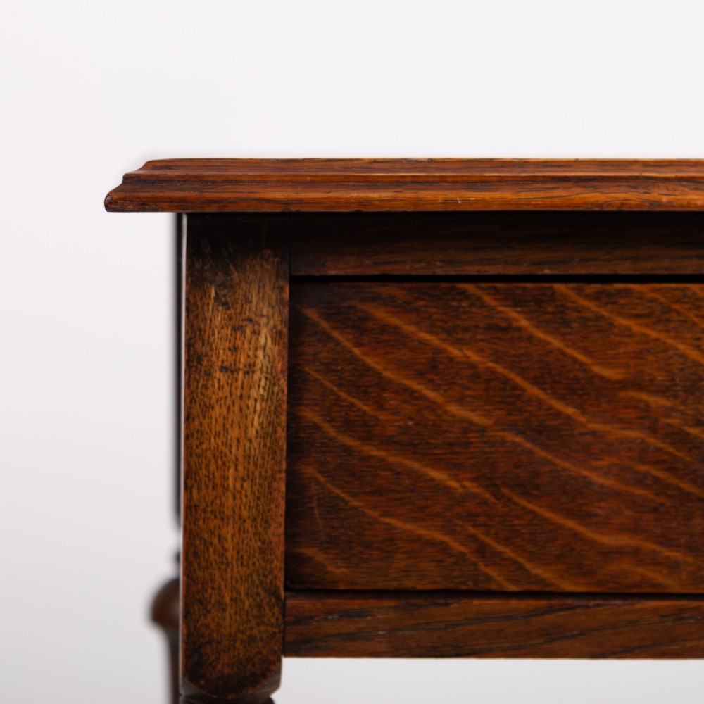 An antique dark oak side table featuring a single drawer with a brass drop ring pull, slender turned legs, and a bobbin stretcher base. View III