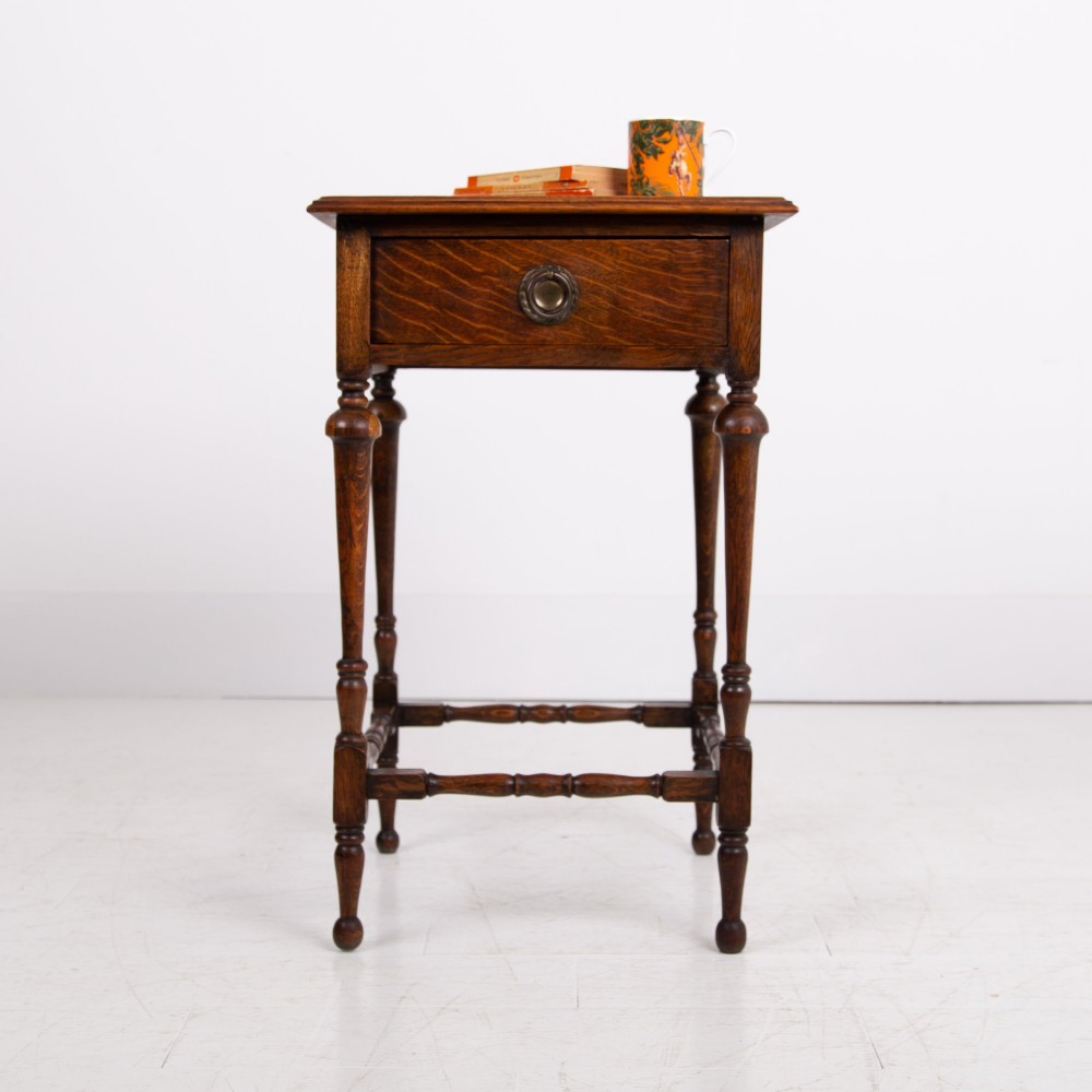 An antique dark oak side table featuring a single drawer with a brass drop ring pull, slender turned legs, and a bobbin stretcher base. View IV