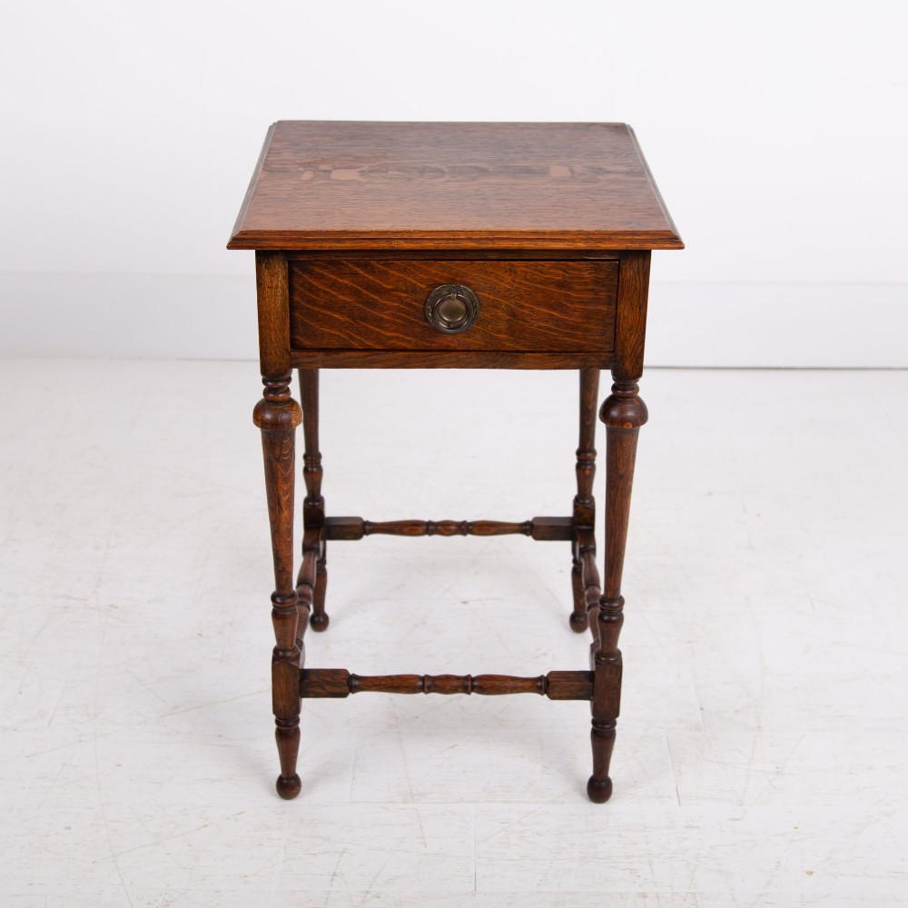 An antique dark oak side table featuring a single drawer with a brass drop ring pull, slender turned legs, and a bobbin stretcher base. View V