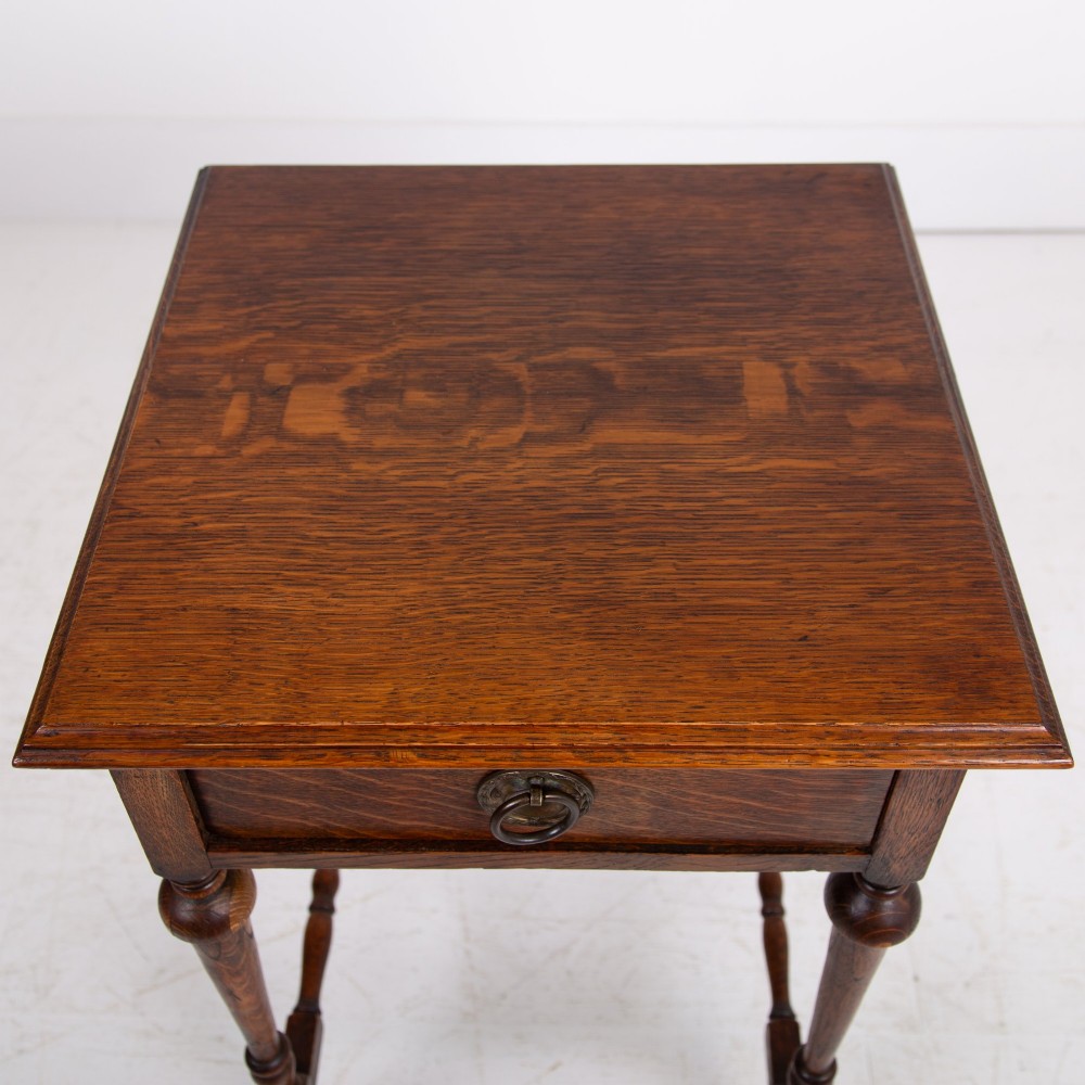 An antique dark oak side table featuring a single drawer with a brass drop ring pull, slender turned legs, and a bobbin stretcher base. View VI