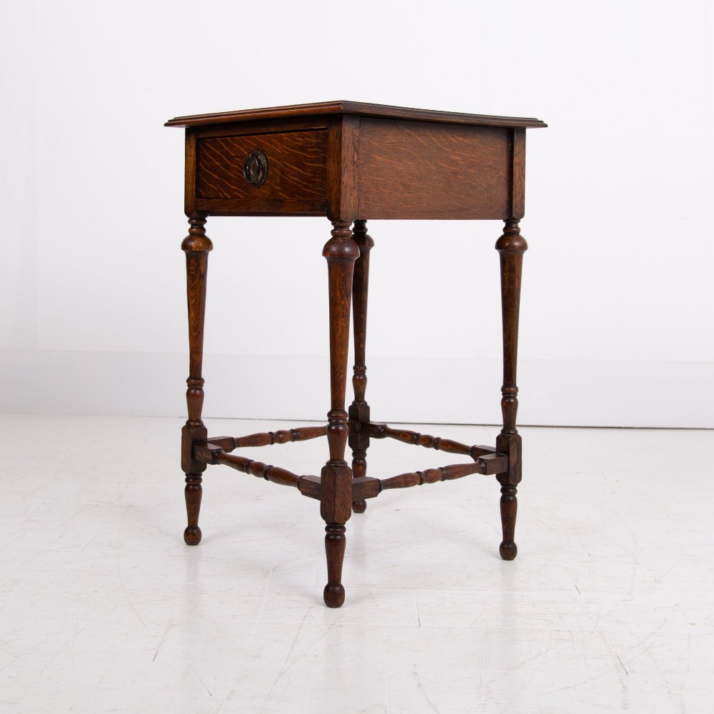An antique dark oak side table featuring a single drawer with a brass drop ring pull, slender turned legs, and a bobbin stretcher base. View XII