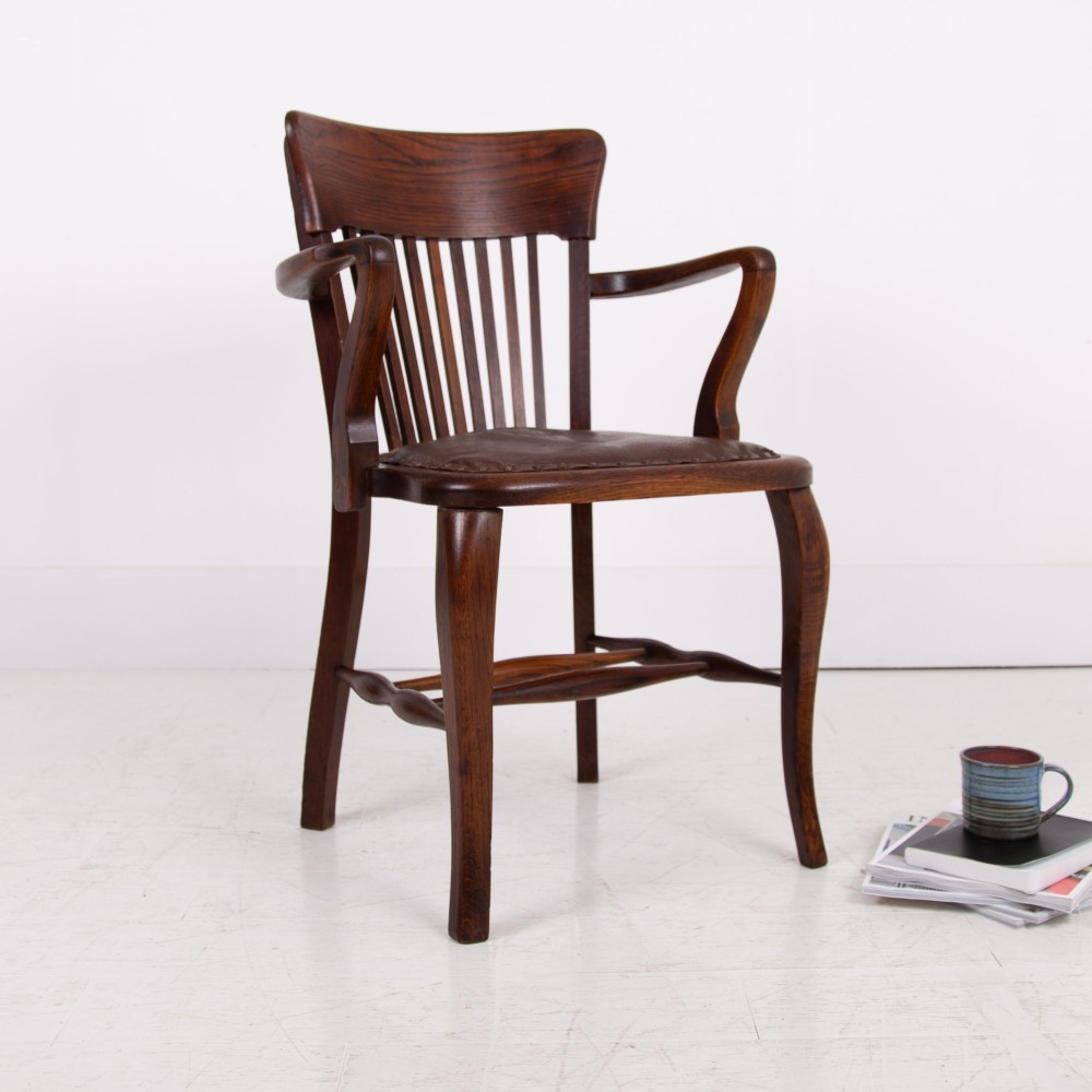 An Edwardian dark oak desk chair featuring a vertical slat backrest, curved armrests, and a studded leather seat.