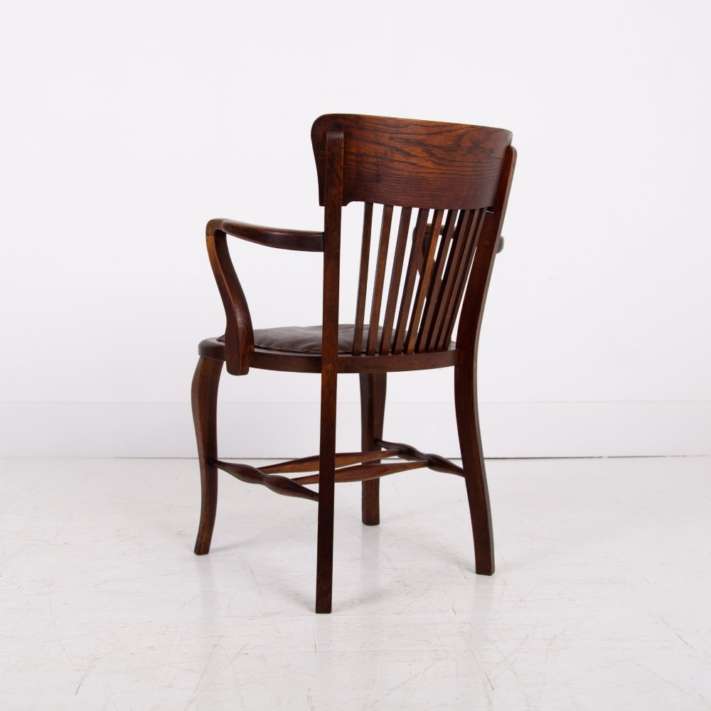 An Edwardian dark oak desk chair featuring a vertical slat backrest, curved armrests, and a studded leather seat. View II