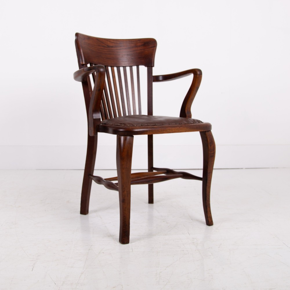 An Edwardian dark oak desk chair featuring a vertical slat backrest, curved armrests, and a studded leather seat. View III