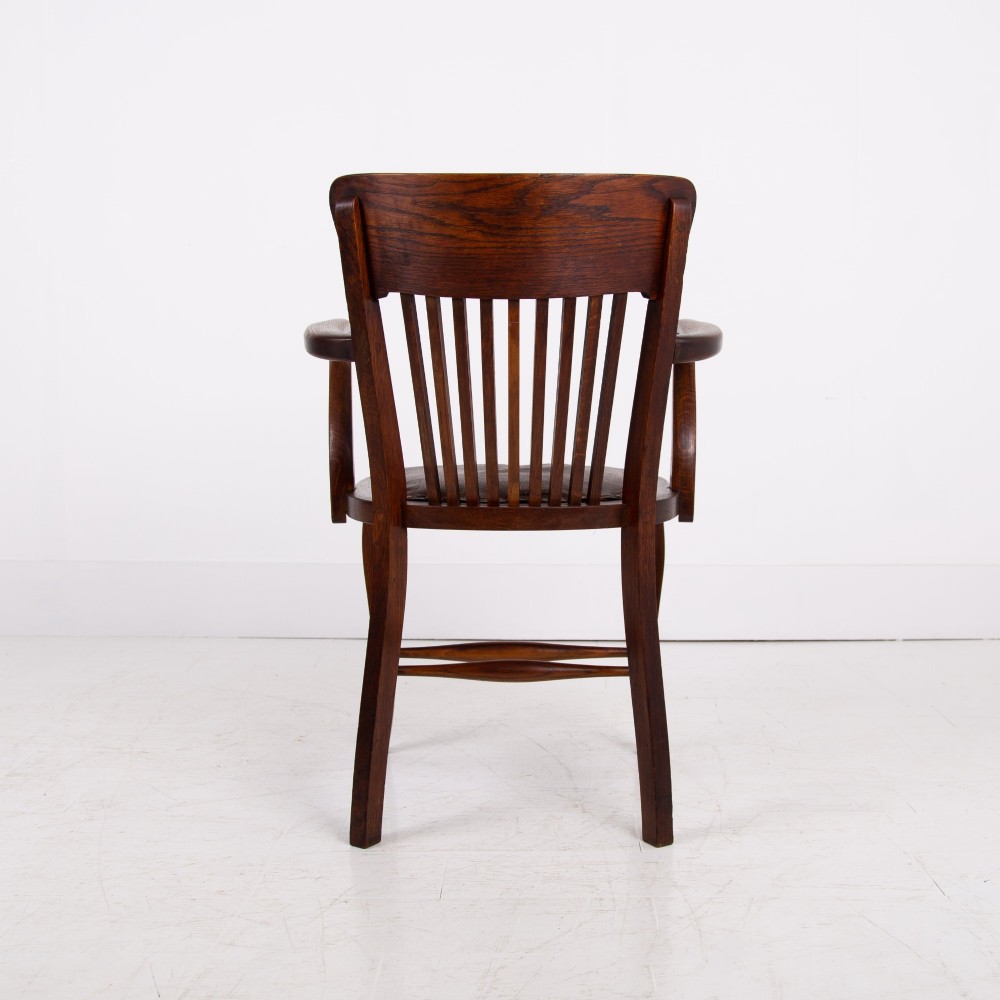 An Edwardian dark oak desk chair featuring a vertical slat backrest, curved armrests, and a studded leather seat. View IV