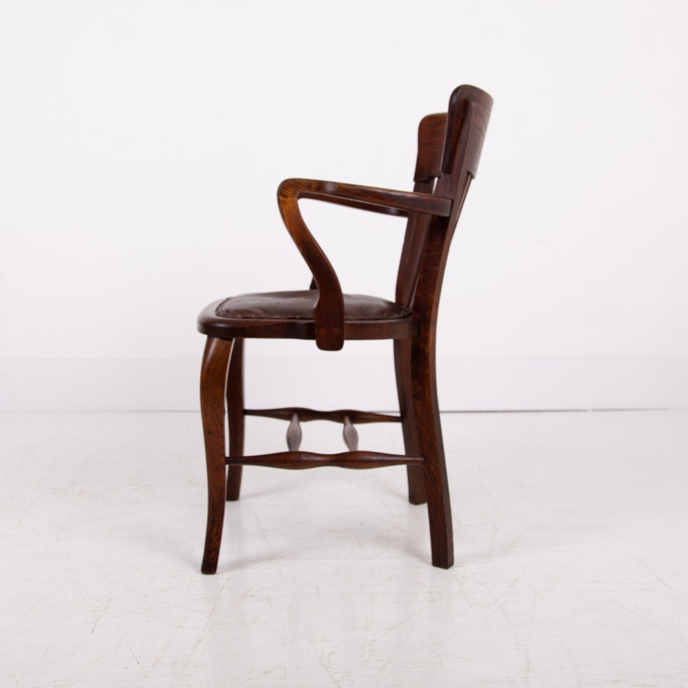 An Edwardian dark oak desk chair featuring a vertical slat backrest, curved armrests, and a studded leather seat. View V