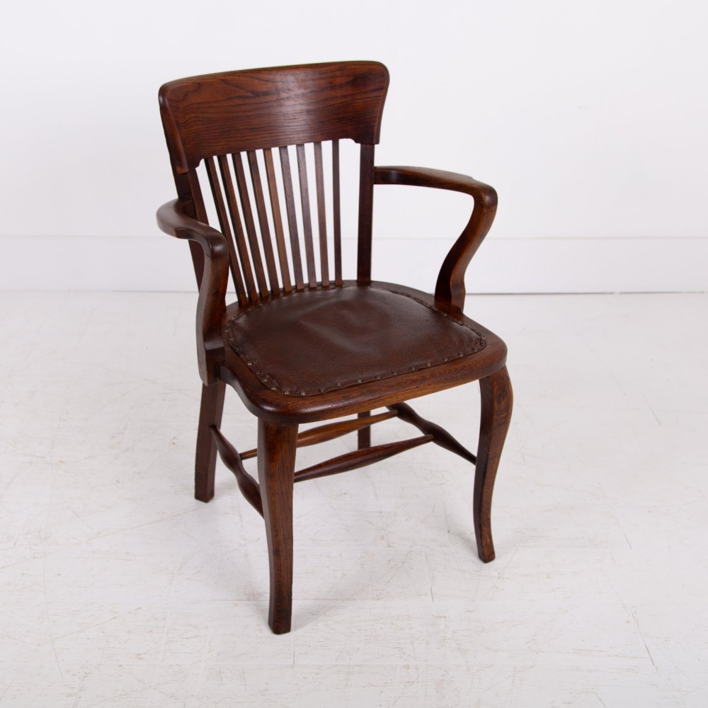 An Edwardian dark oak desk chair featuring a vertical slat backrest, curved armrests, and a studded leather seat. View VI