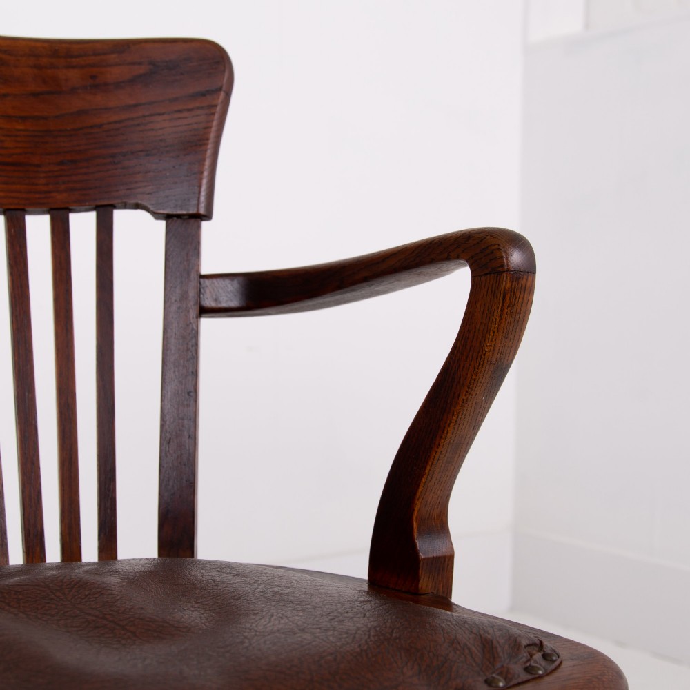 An Edwardian dark oak desk chair featuring a vertical slat backrest, curved armrests, and a studded leather seat. View VIII