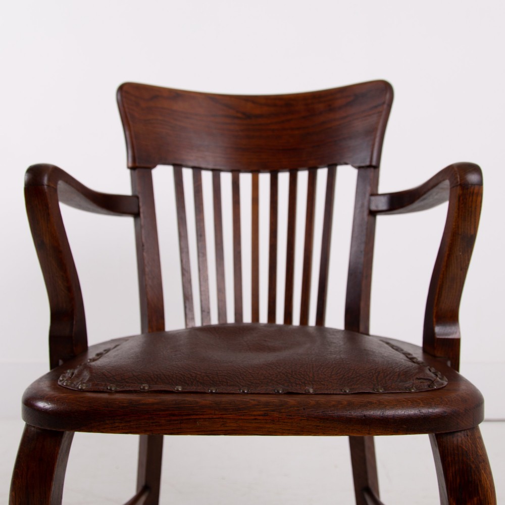 An Edwardian dark oak desk chair featuring a vertical slat backrest, curved armrests, and a studded leather seat. View IX