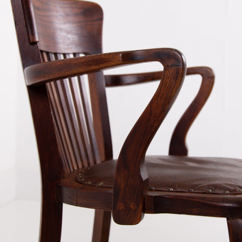 An Edwardian dark oak desk chair featuring a vertical slat backrest, curved armrests, and a studded leather seat. View X