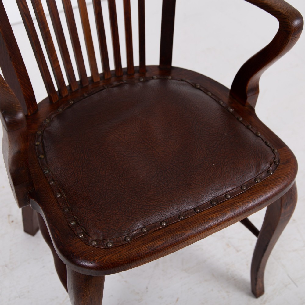An Edwardian dark oak desk chair featuring a vertical slat backrest, curved armrests, and a studded leather seat. View XI