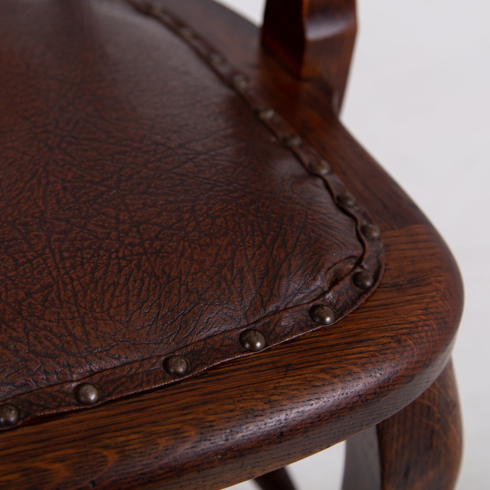 An Edwardian dark oak desk chair featuring a vertical slat backrest, curved armrests, and a studded leather seat. View XII