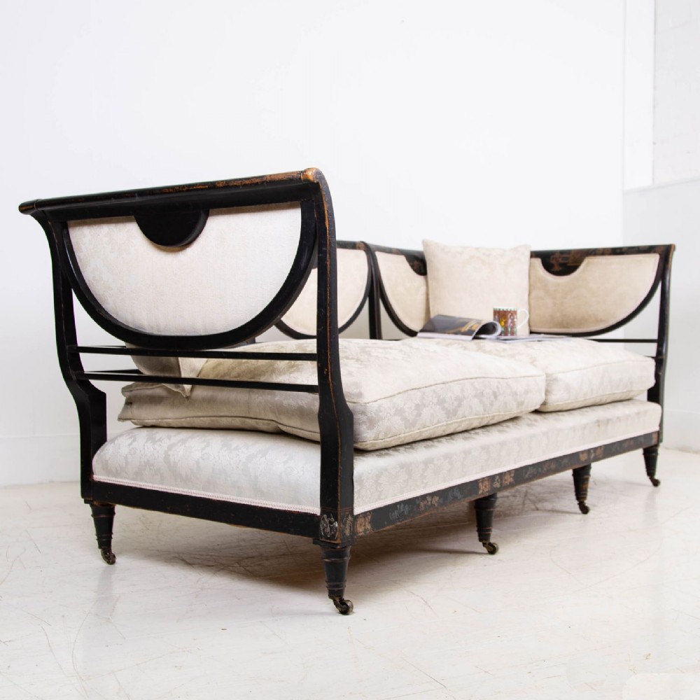 A Victorian Chinoiserie sofa with a black lacquered frame featuring gilt painted details, semicircular cream patterned back panels, and cream upholstered seat cushions. View X