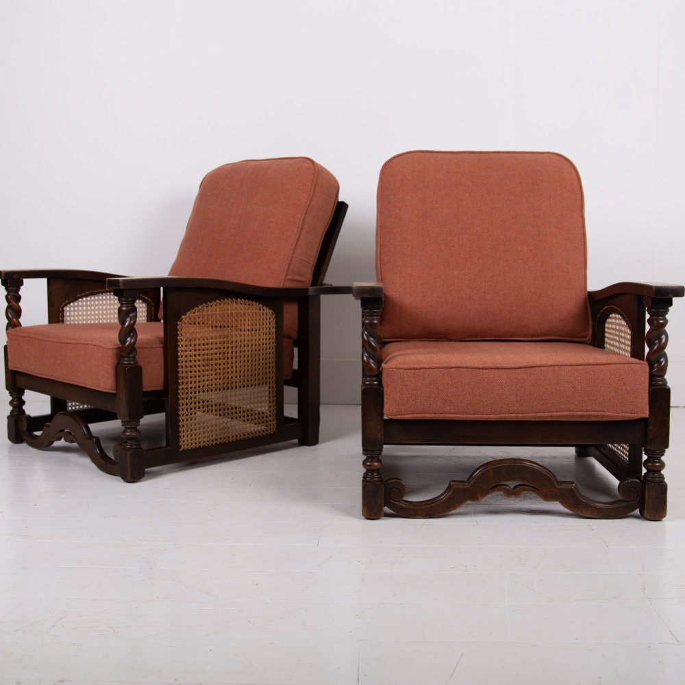 A pair of 1920s dark oak armchairs featuring barley twist supports, woven cane side panels, and terracotta upholstered cushions.