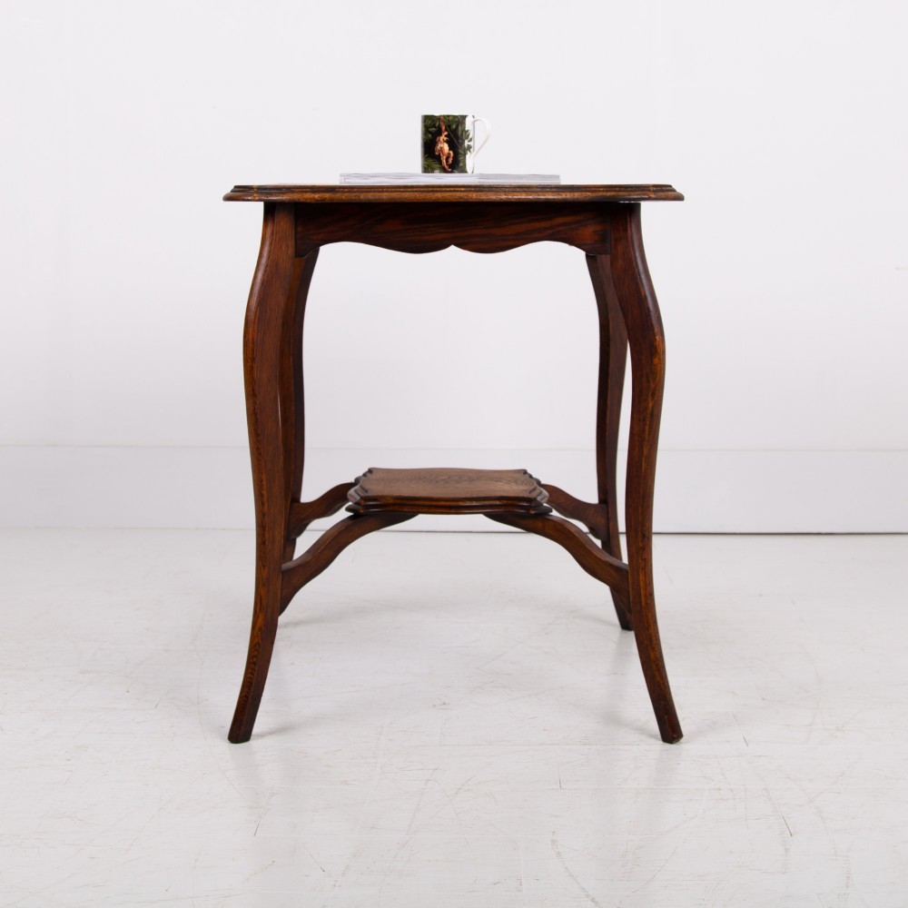 An Edwardian oak occasional table featuring a serpentine-shaped top surface, four slender cabriole legs, and a matching lower shelf. View IV