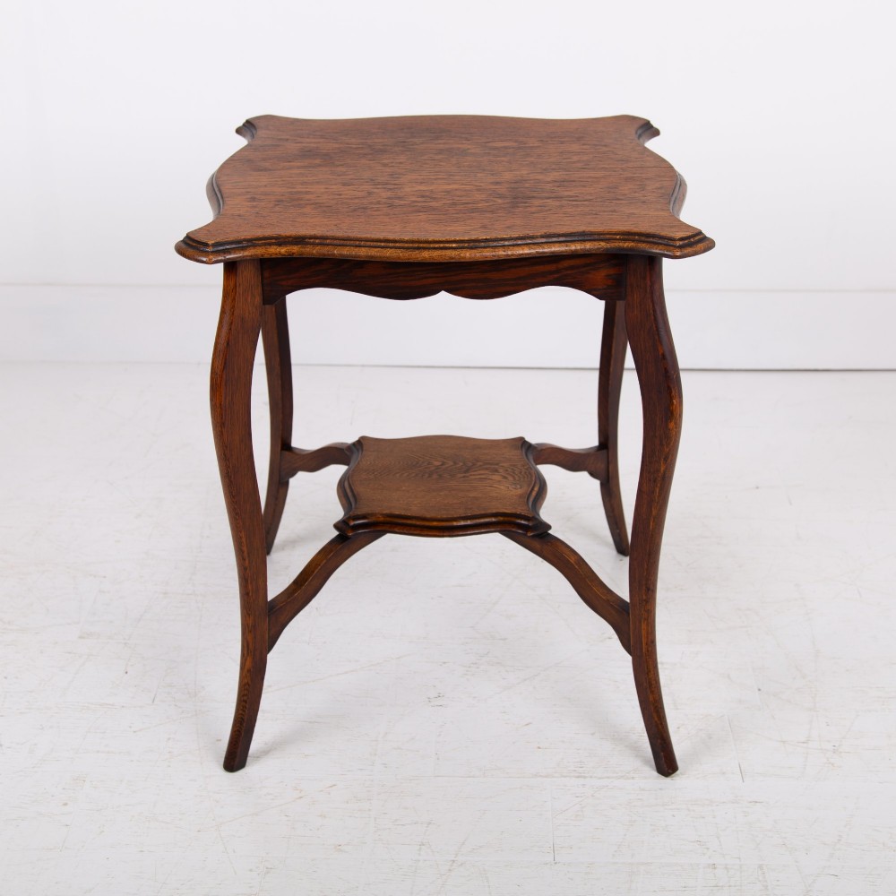 An Edwardian oak occasional table featuring a serpentine-shaped top surface, four slender cabriole legs, and a matching lower shelf.