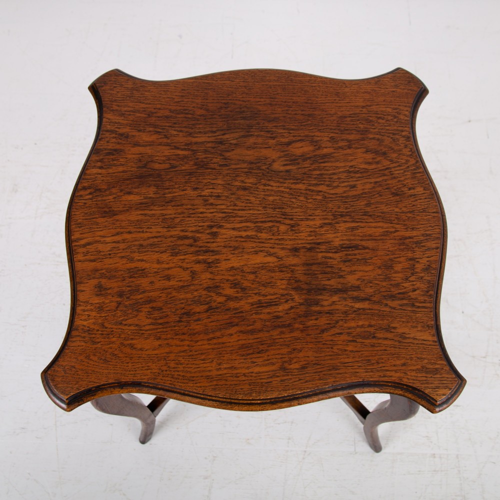 An Edwardian oak occasional table featuring a serpentine-shaped top surface, four slender cabriole legs, and a matching lower shelf. View VII