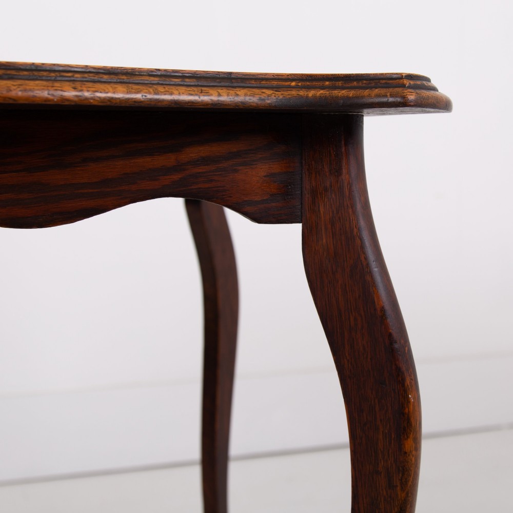 An Edwardian oak occasional table featuring a serpentine-shaped top surface, four slender cabriole legs, and a matching lower shelf. View X