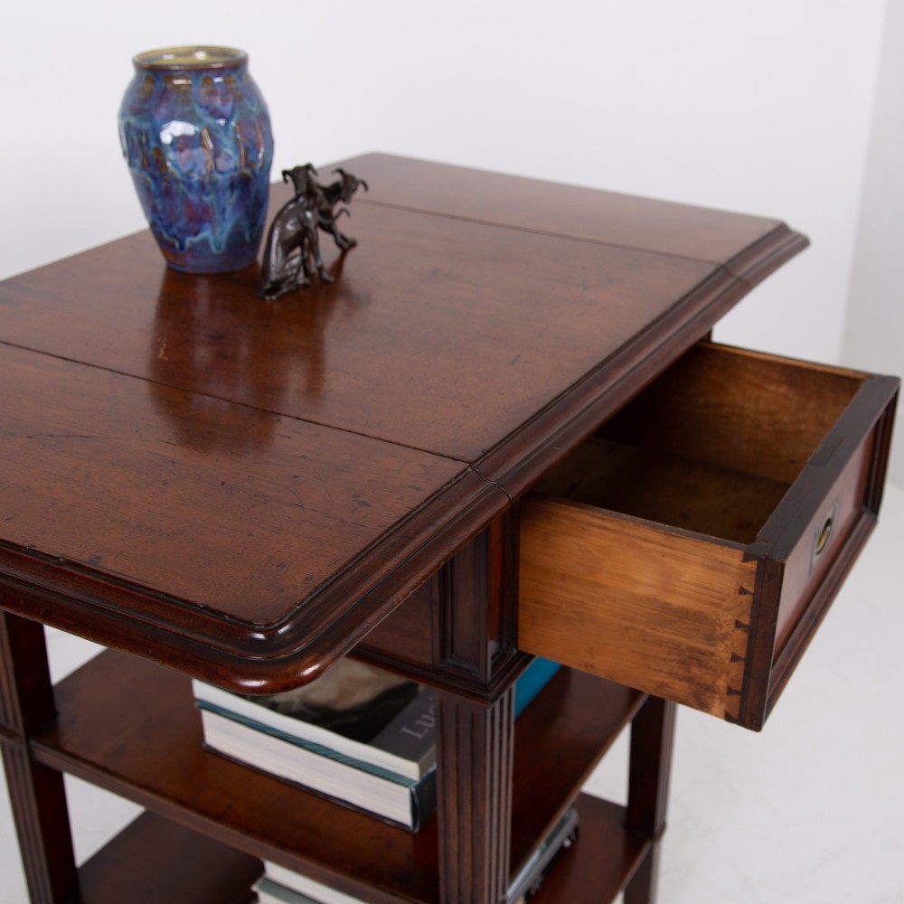 A late nineteenth-century dark mahogany drop-leaf table featuring a single top drawer with a brass pull, two lower open shelves, and fluted legs. View V