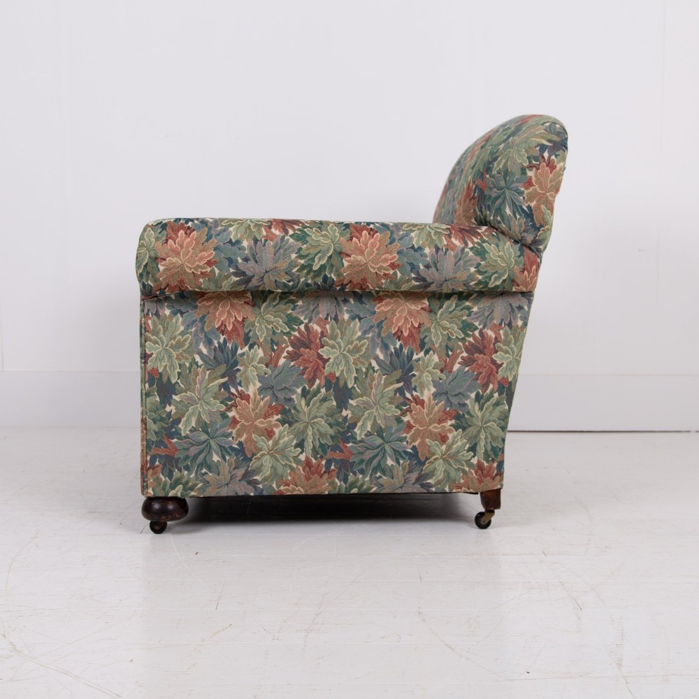 A pair of early 20th-century English upholstered armchairs featuring a multi-coloured botanical leaf pattern, deep seats, rolled arms, and turned feet on castors. View II