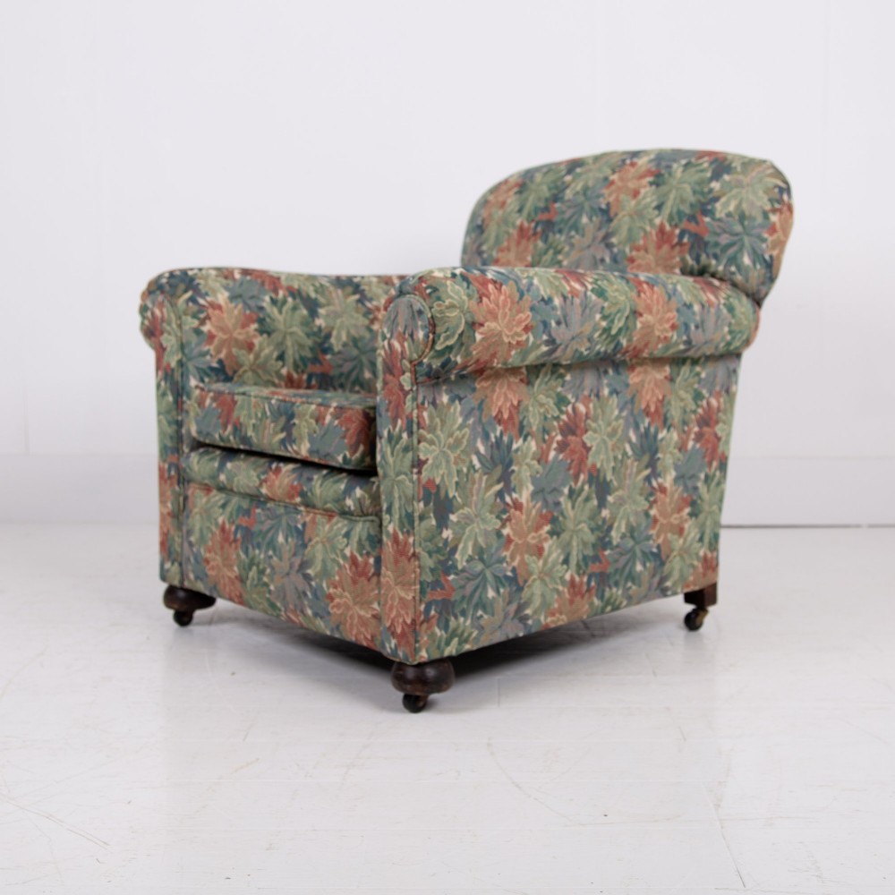A pair of early 20th-century English upholstered armchairs featuring a multi-coloured botanical leaf pattern, deep seats, rolled arms, and turned feet on castors. View III