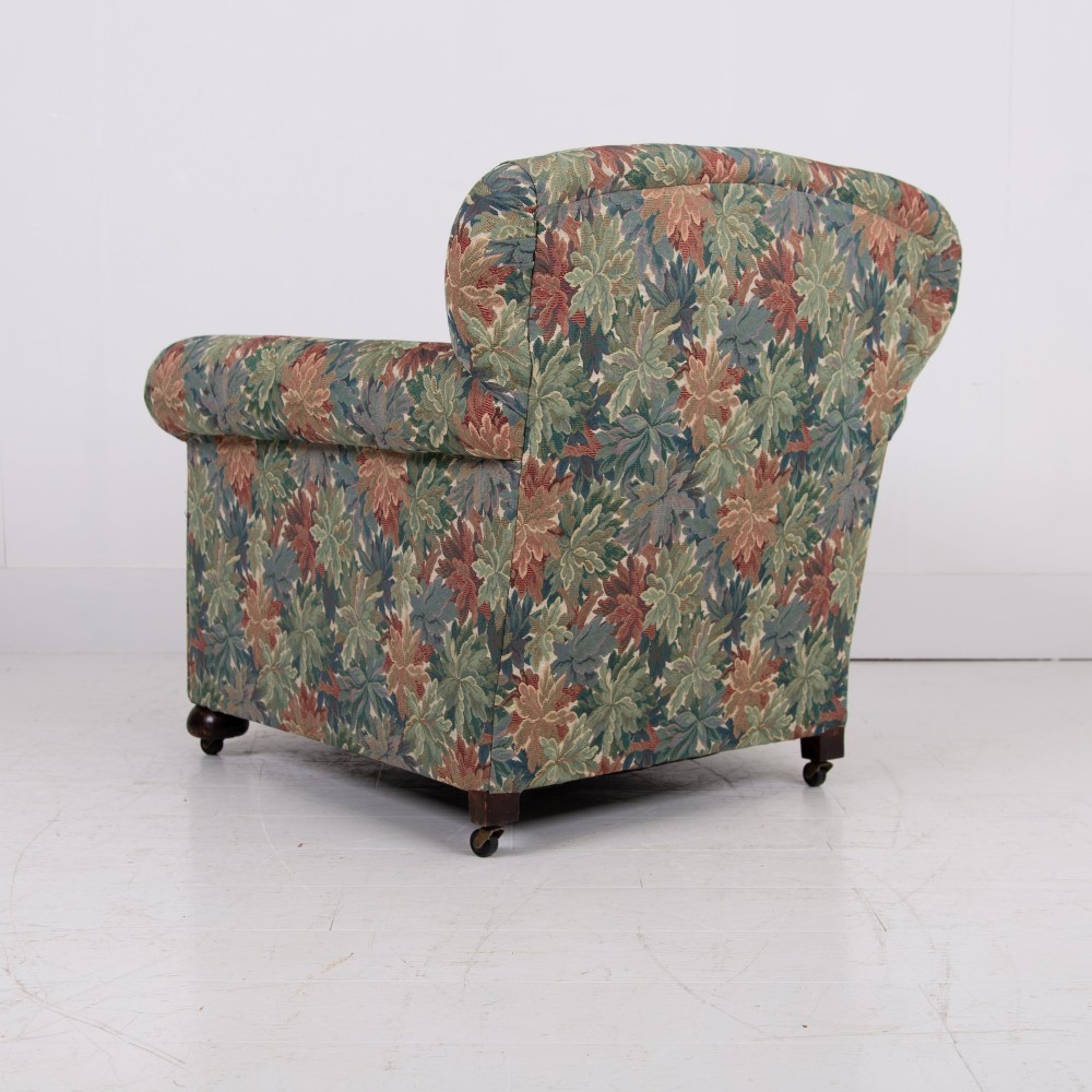 A pair of early 20th-century English upholstered armchairs featuring a multi-coloured botanical leaf pattern, deep seats, rolled arms, and turned feet on castors. View V
