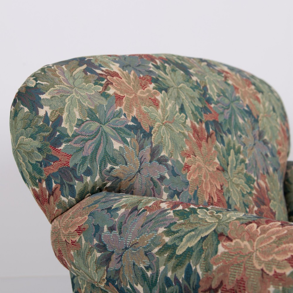 A pair of early 20th-century English upholstered armchairs featuring a multi-coloured botanical leaf pattern, deep seats, rolled arms, and turned feet on castors. View VI