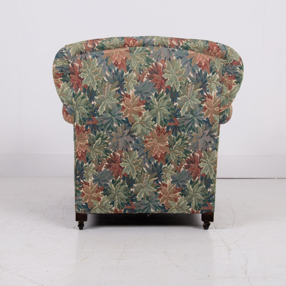 A pair of early 20th-century English upholstered armchairs featuring a multi-coloured botanical leaf pattern, deep seats, rolled arms, and turned feet on castors. View VIII