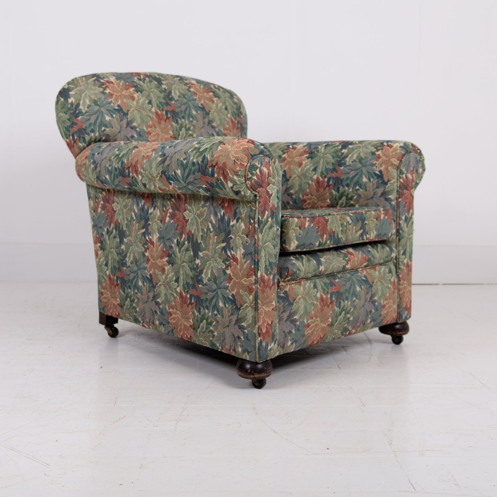 A pair of early 20th-century English upholstered armchairs featuring a multi-coloured botanical leaf pattern, deep seats, rolled arms, and turned feet on castors. View IX
