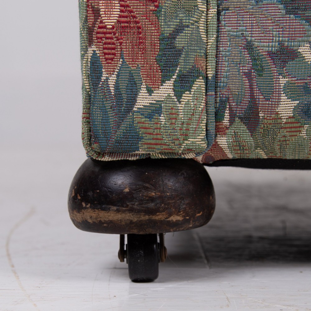 A pair of early 20th-century English upholstered armchairs featuring a multi-coloured botanical leaf pattern, deep seats, rolled arms, and turned feet on castors. View X