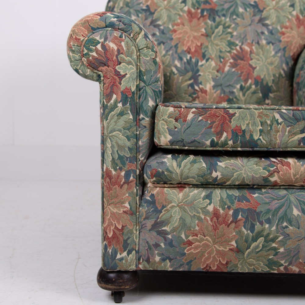 A pair of early 20th-century English upholstered armchairs featuring a multi-coloured botanical leaf pattern, deep seats, rolled arms, and turned feet on castors. View XI
