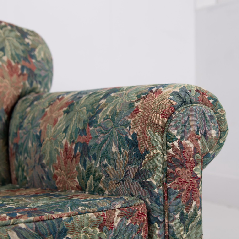 A pair of early 20th-century English upholstered armchairs featuring a multi-coloured botanical leaf pattern, deep seats, rolled arms, and turned feet on castors. View XII