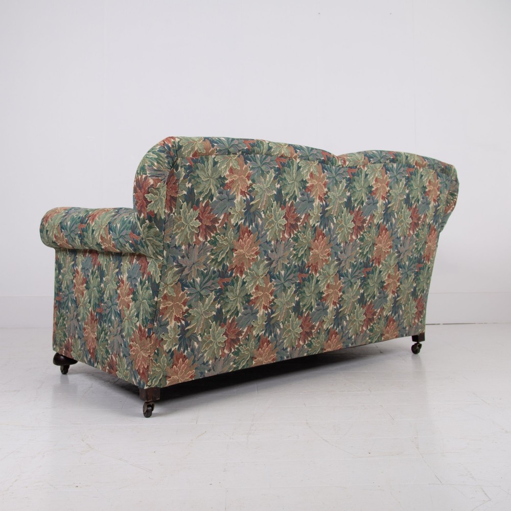 An Edwardian two-seater sofa upholstered in a multi-coloured leaf tapestry fabric with rolled arms and turned timber legs on casters. View III