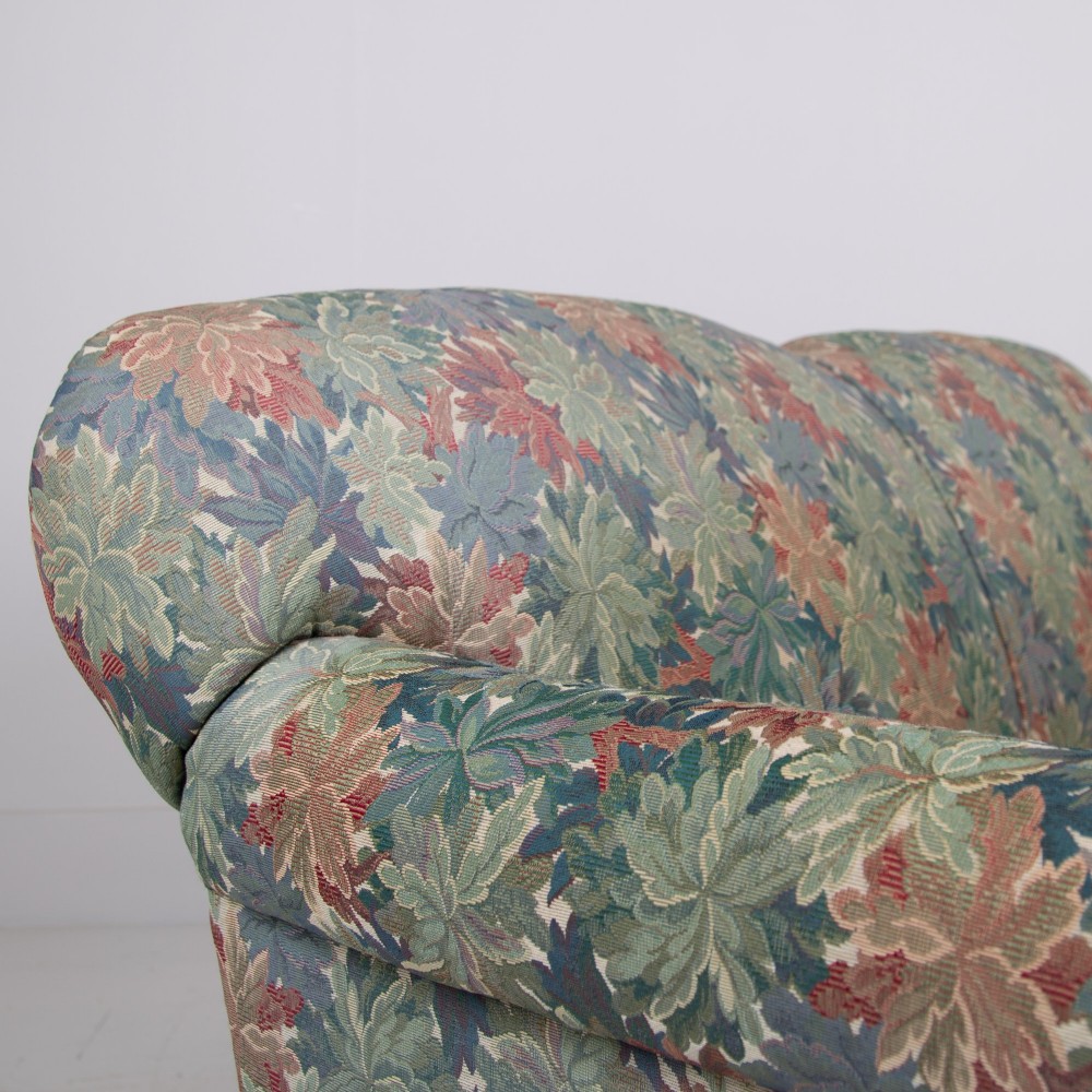 An Edwardian two-seater sofa upholstered in a multi-coloured leaf tapestry fabric with rolled arms and turned timber legs on casters. View V