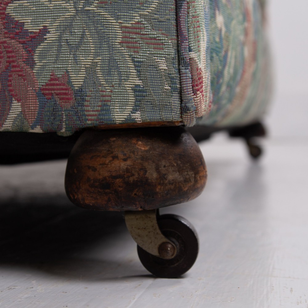 An Edwardian two-seater sofa upholstered in a multi-coloured leaf tapestry fabric with rolled arms and turned timber legs on casters. View VI