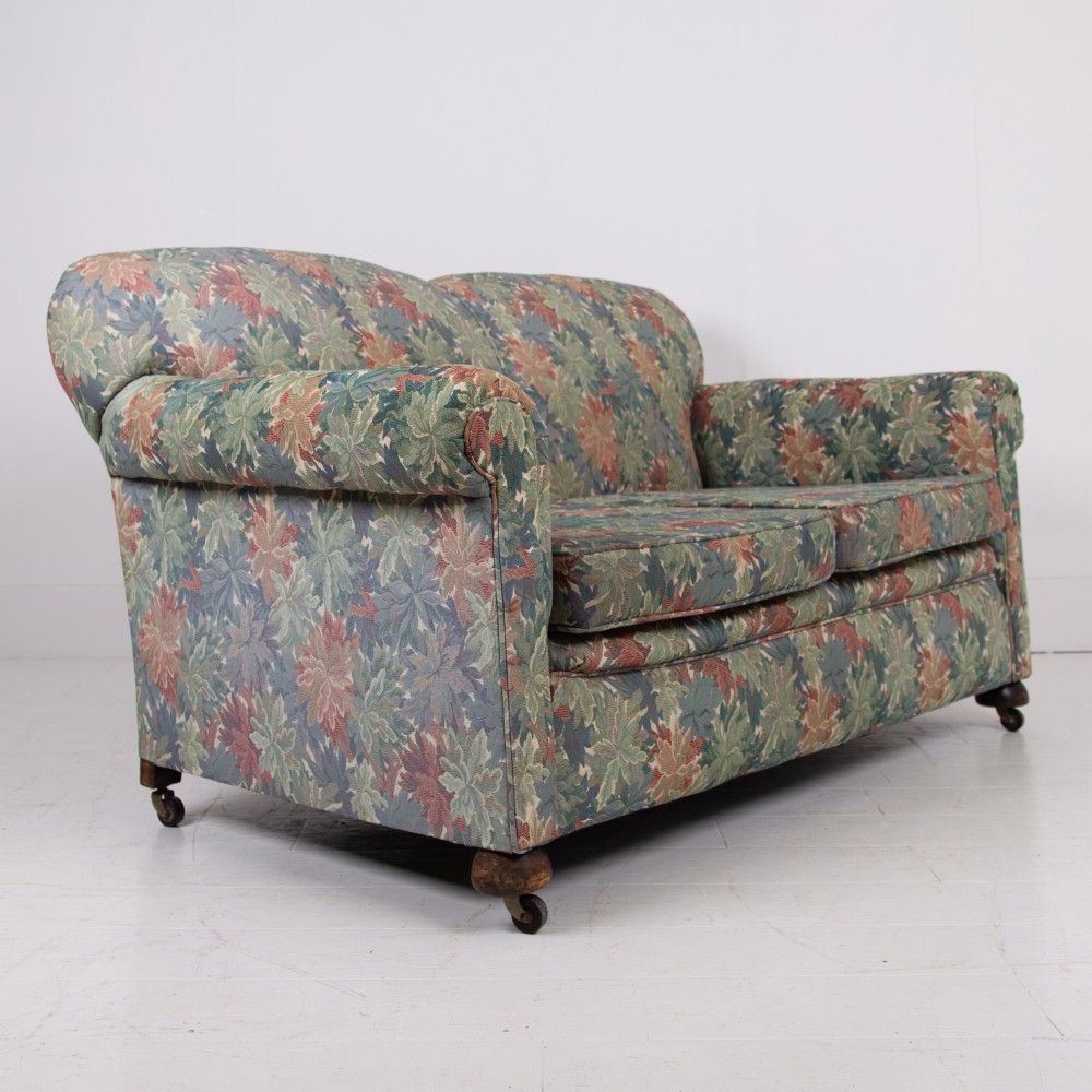An Edwardian two-seater sofa upholstered in a multi-coloured leaf tapestry fabric with rolled arms and turned timber legs on casters. View VIII