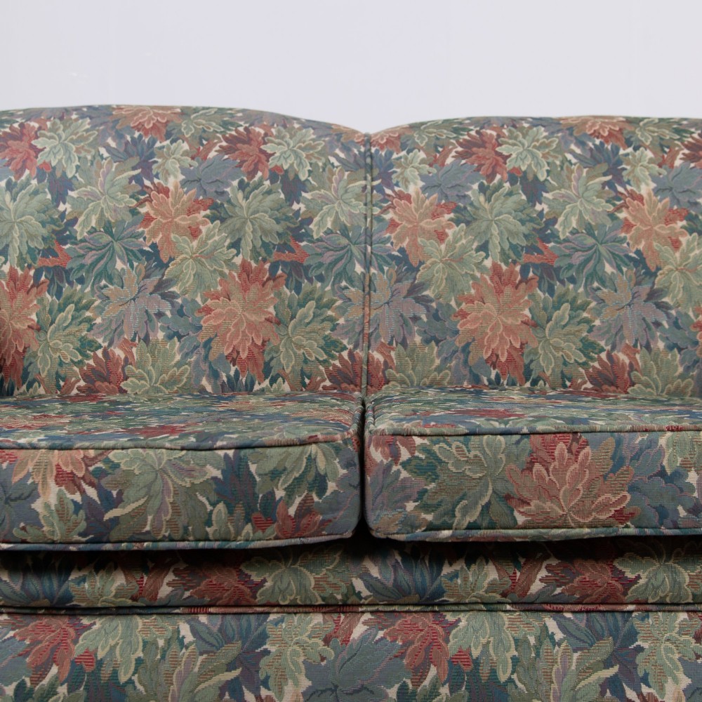 An Edwardian two-seater sofa upholstered in a multi-coloured leaf tapestry fabric with rolled arms and turned timber legs on casters. View IX