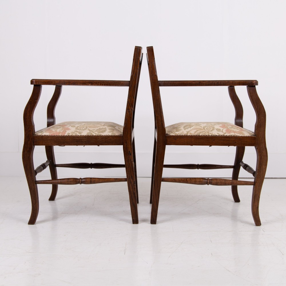 A pair of dark oak open armchairs featuring carved floral back splats, curved arms, turned stretchers, and light floral upholstered seats. View II