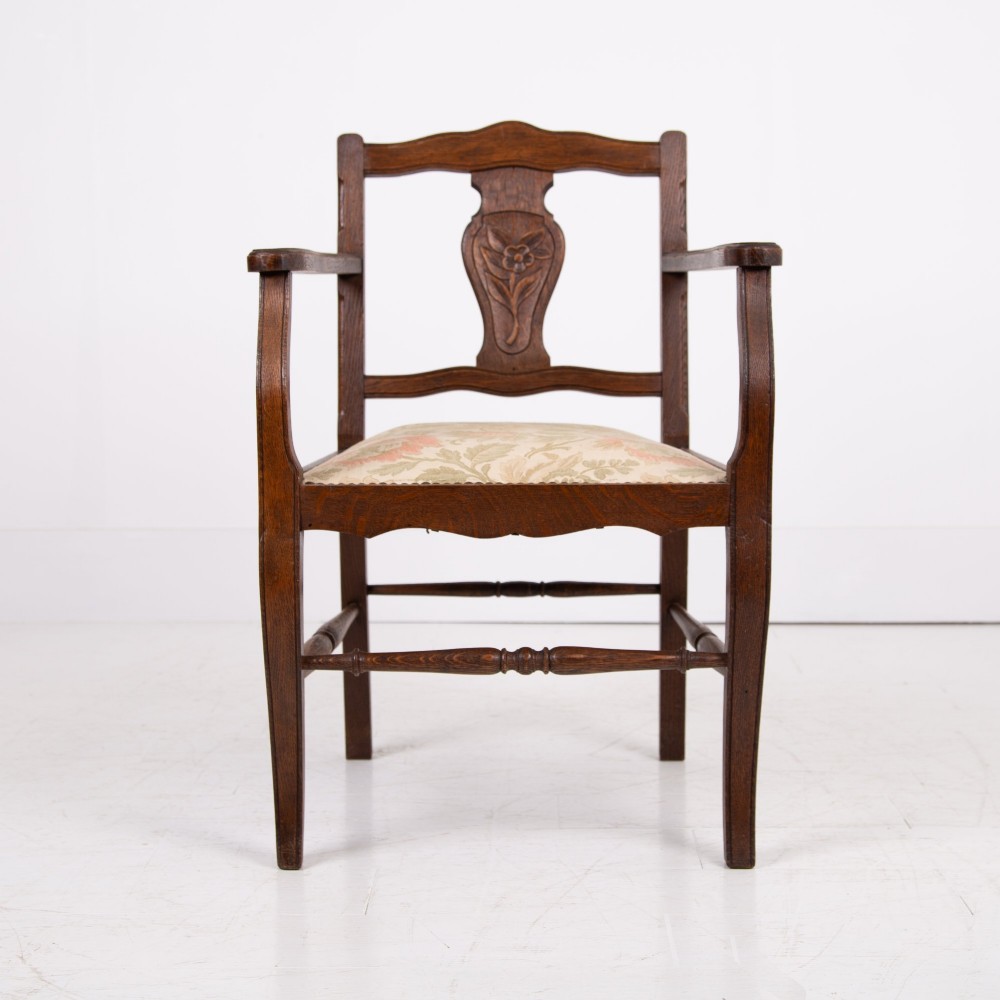 A pair of dark oak open armchairs featuring carved floral back splats, curved arms, turned stretchers, and light floral upholstered seats. View V