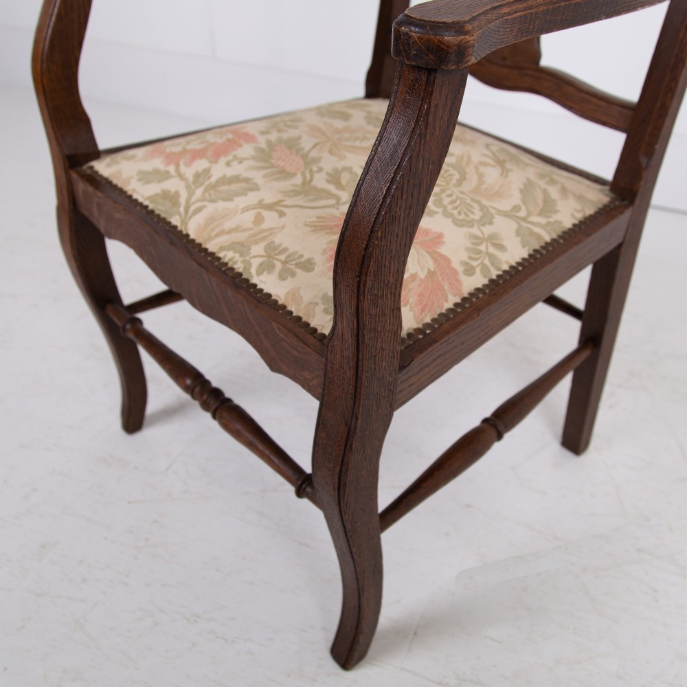A pair of dark oak open armchairs featuring carved floral back splats, curved arms, turned stretchers, and light floral upholstered seats. View X